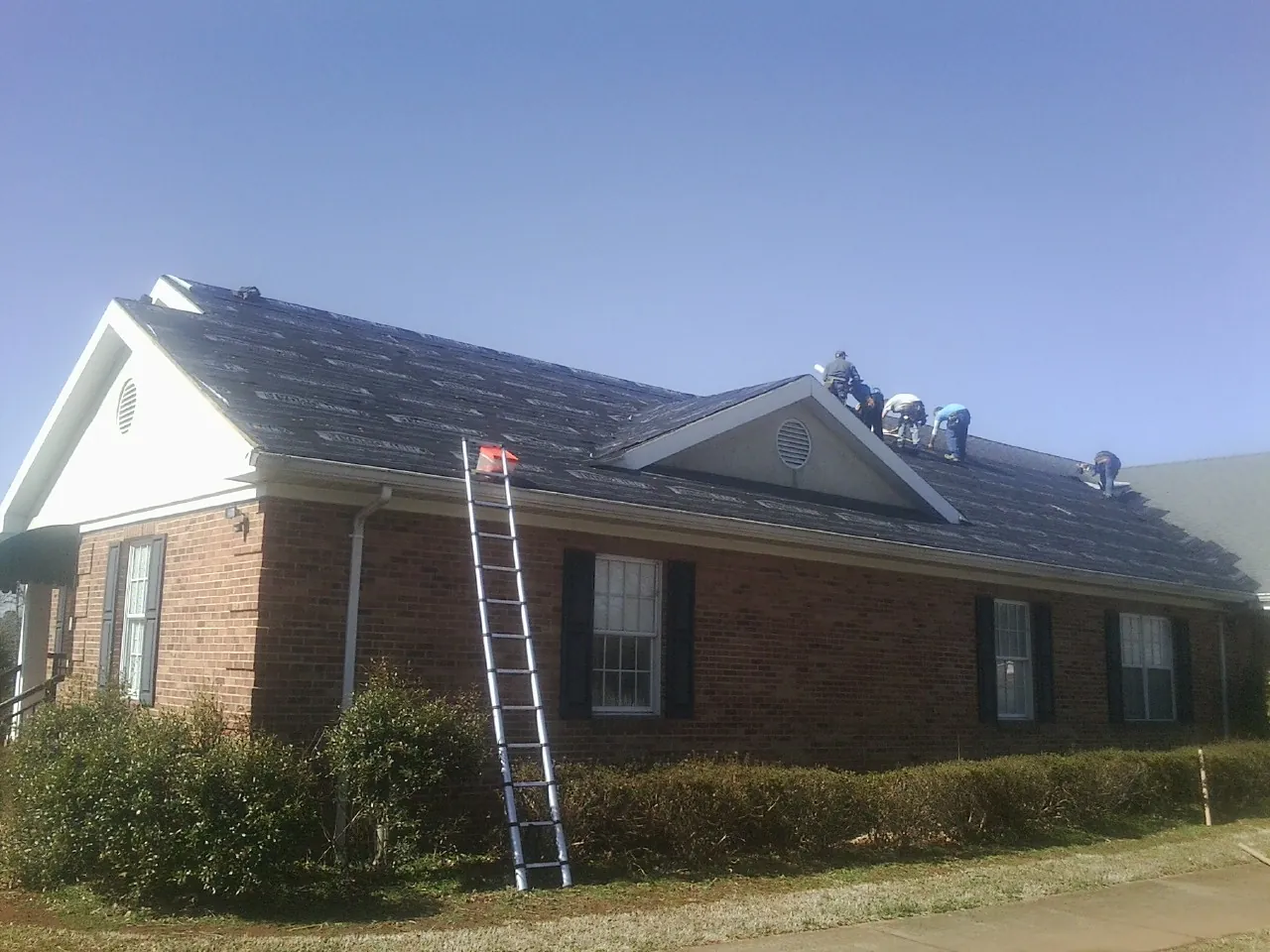 Crew tearing shingles off a brick ranch roof with a ladder set — Emergency Roof Repair work by our crew in Ashaway