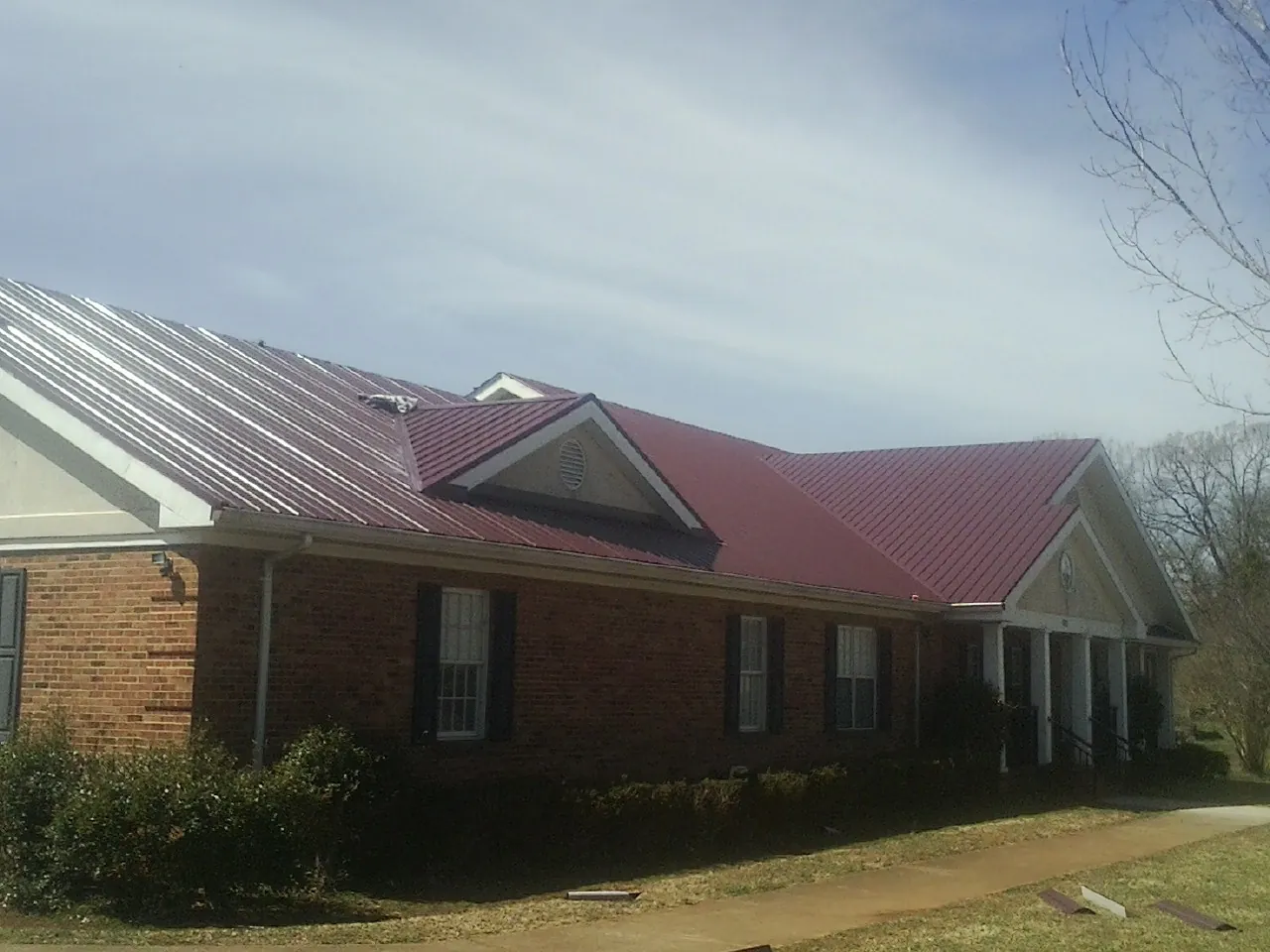 Red metal roof with gabled entries on a long brick building, from a Hail Damage Roof Repair job in Ashaway