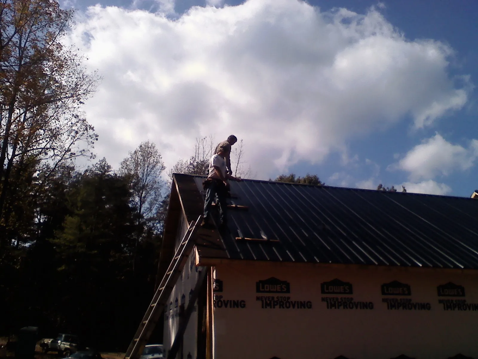 Roofer fastening dark metal panels high against a cloudy sky, from a Roof Inspection job in Ashaway