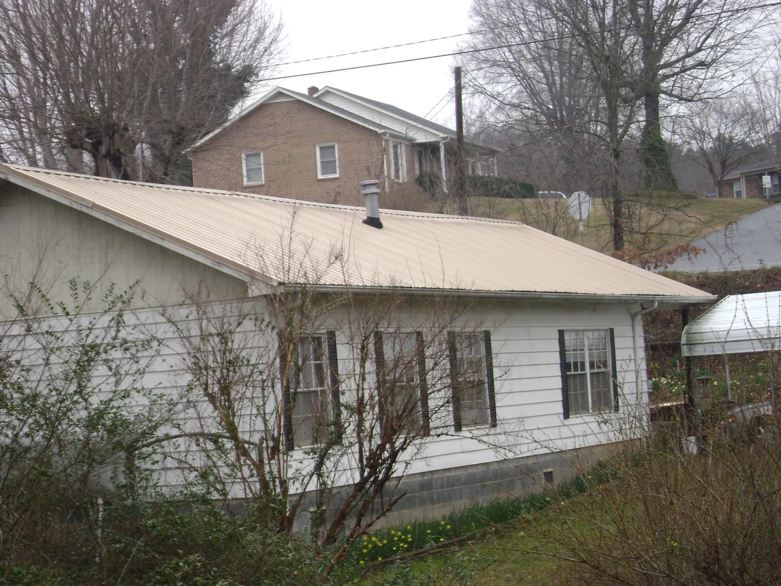 Tan metal roof on a white sided house set into a hillside — Commercial Roofing by Roofing Brothers in Ashaway